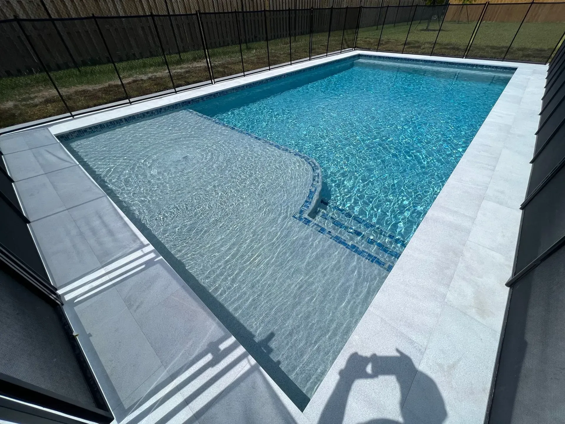 Rectangular swimming pool with light blue water and steps. Gray tile surrounding the pool.
