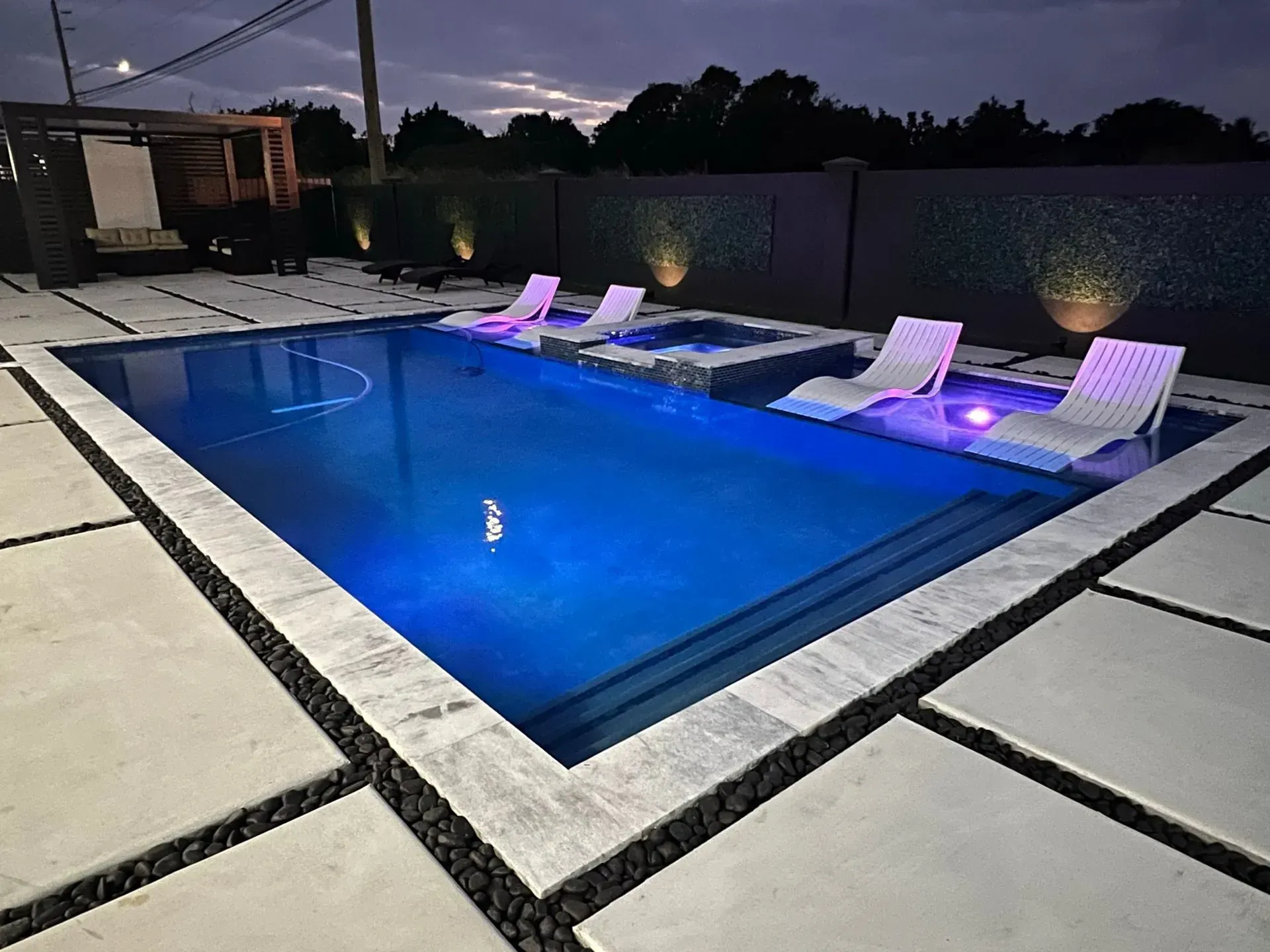 Night view of a luxurious swimming pool with illuminated chairs, set in a modern outdoor space.