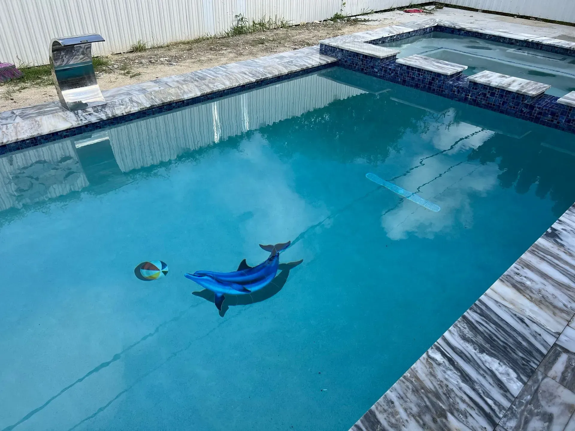 Swimming pool with blue water; a dolphin and fish float. Stone patio surrounds.