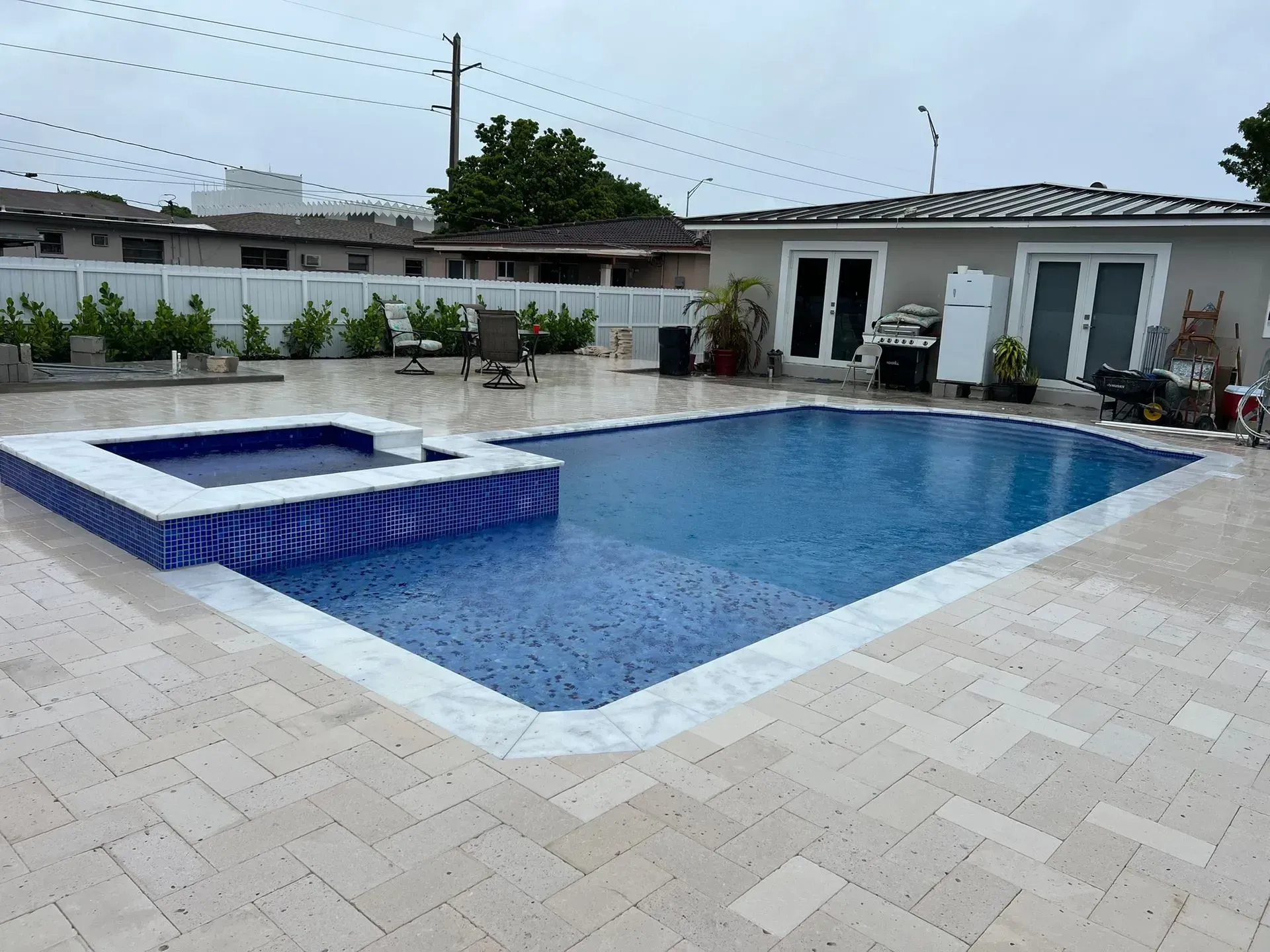 Backyard pool and hot tub with blue tiles, surrounded by light-colored paving stones.