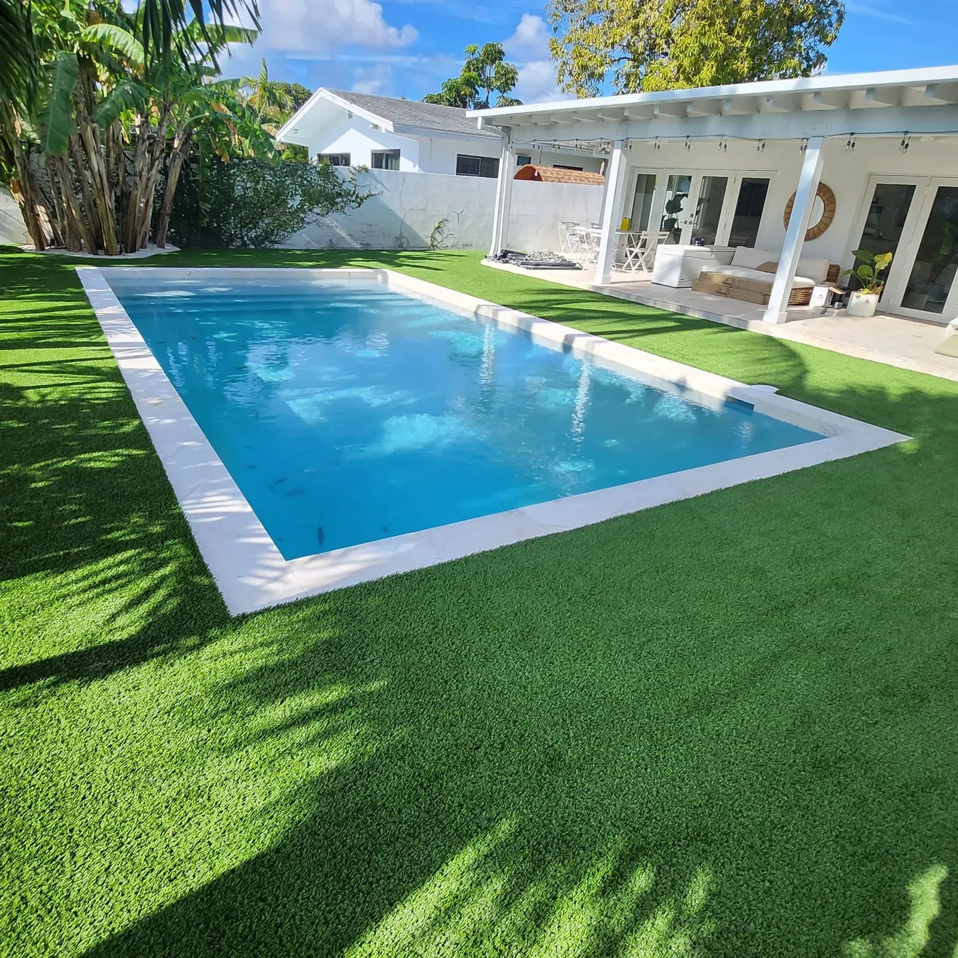 Rectangular pool surrounded by artificial green turf; white patio with seating area.