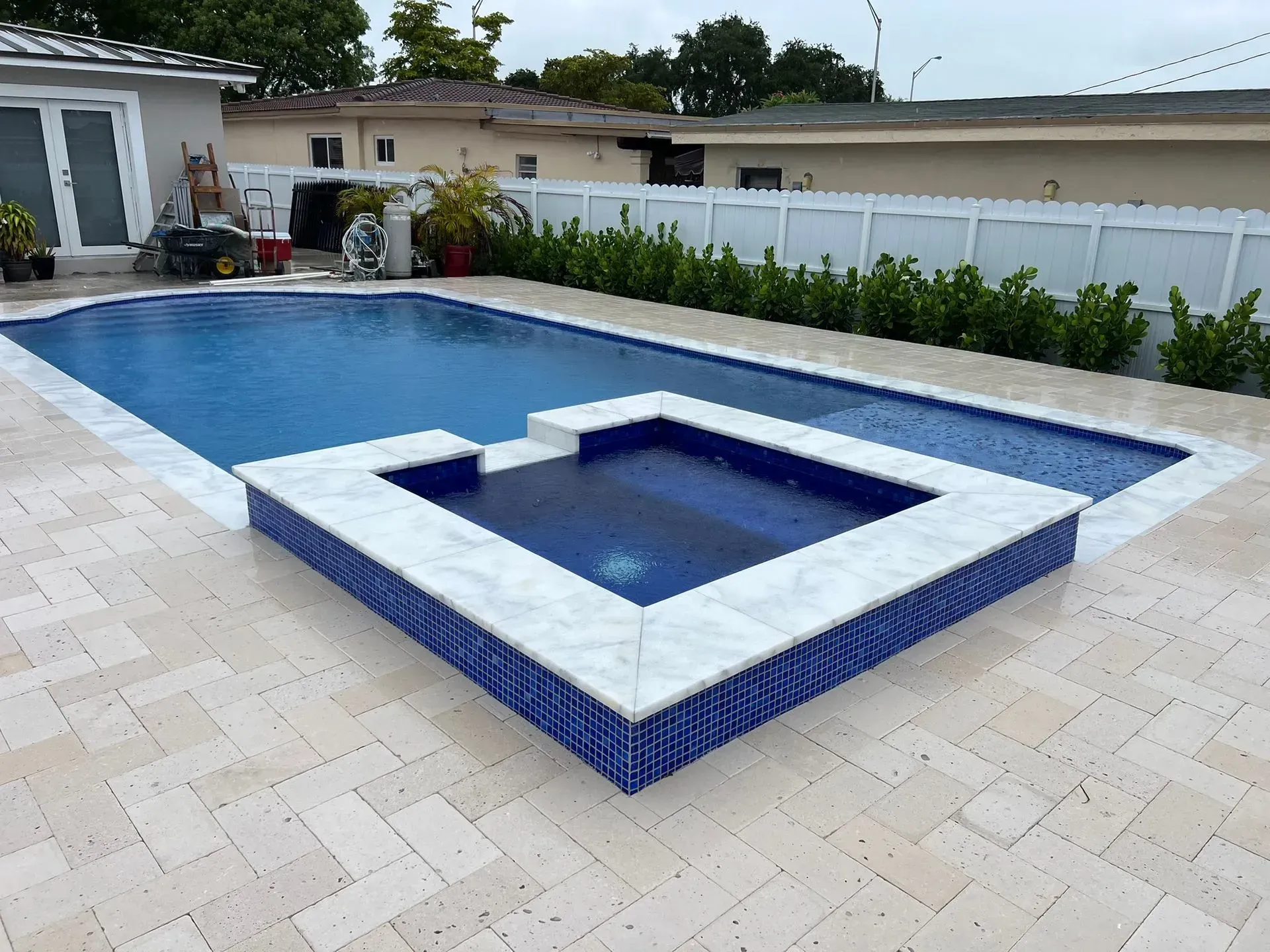 Rectangular pool with attached spa, blue tile, white coping, tan patio, and green hedges.