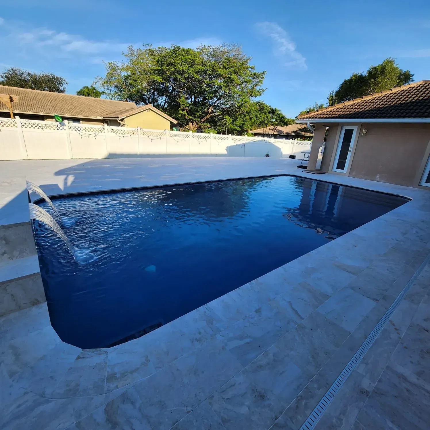 Rectangular pool filled with dark blue water surrounded by light stone patio and building.