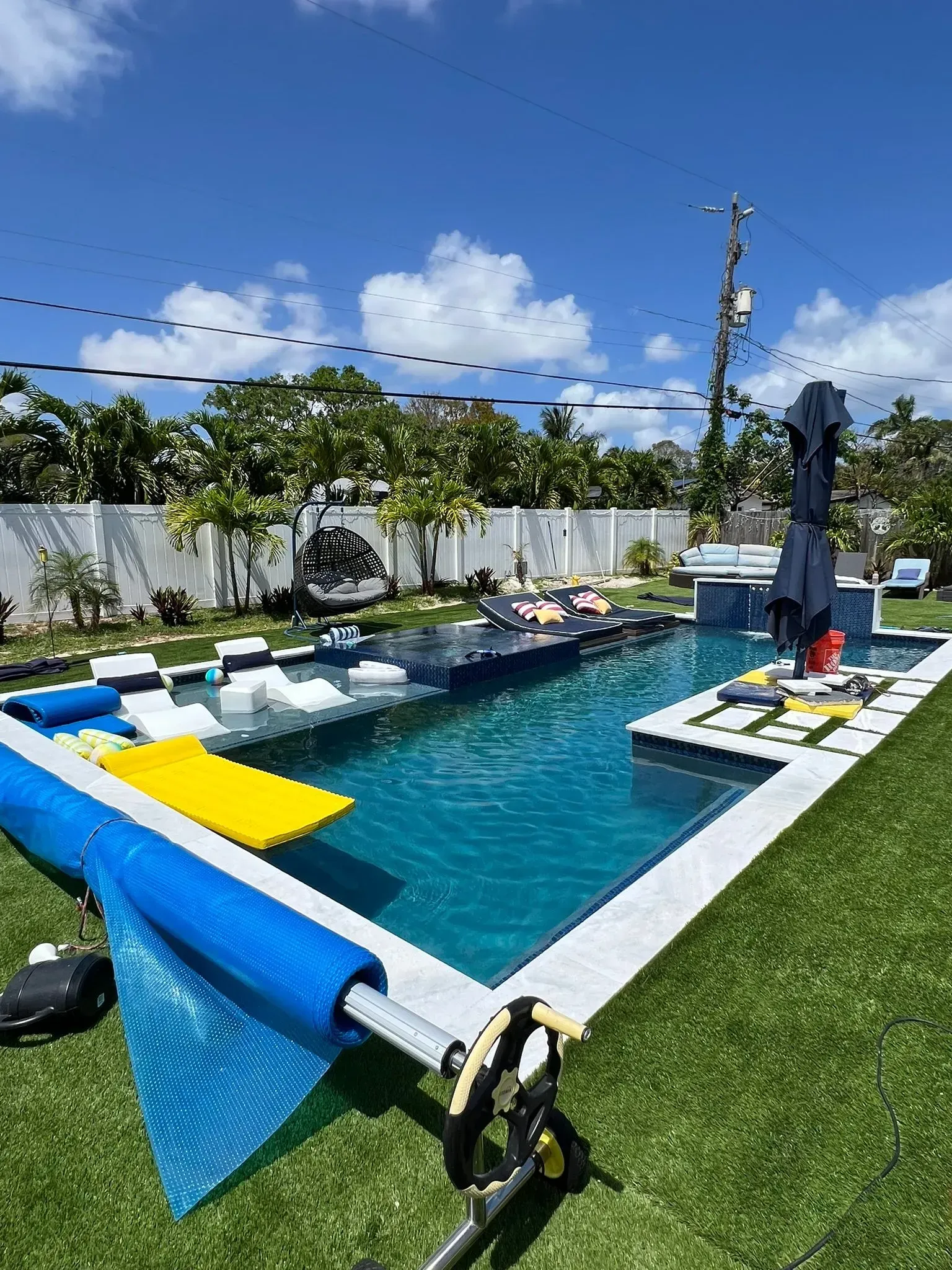 Swimming pool with blue water, white tiles, and green turf lawn under a blue sky.