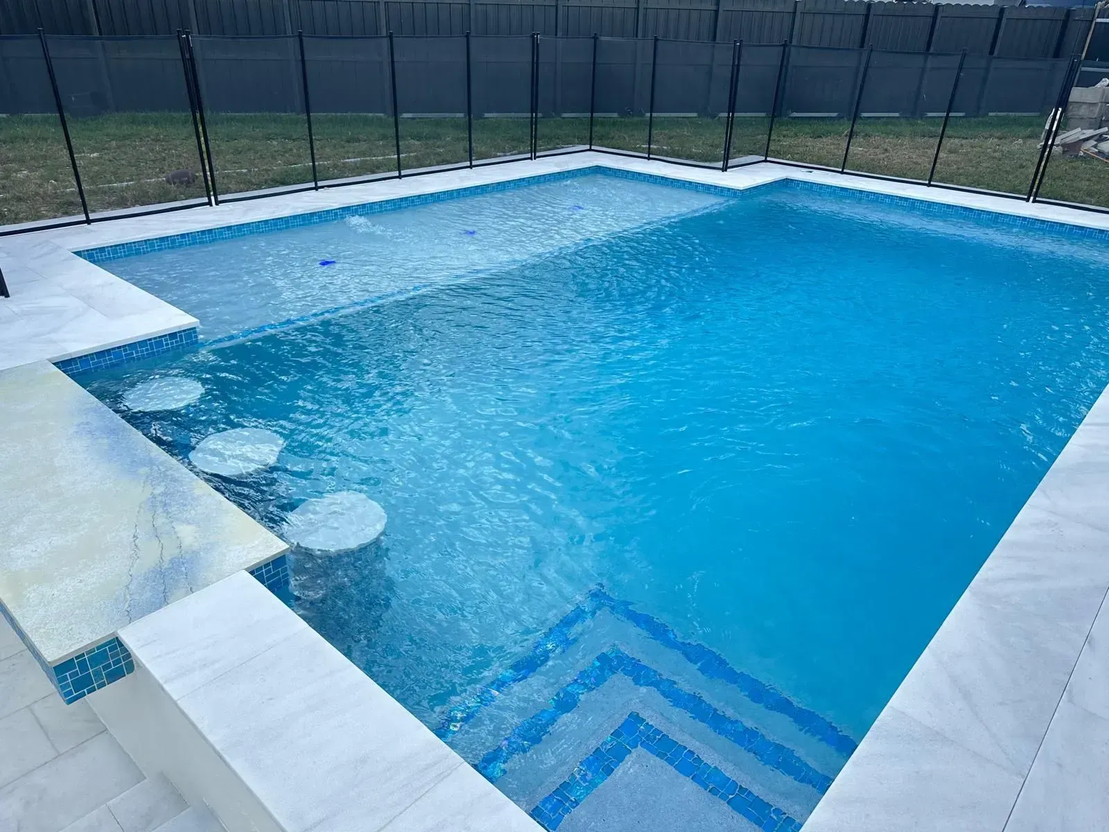 Pool with clear blue water and steps, swim-up bar, and safety fence.