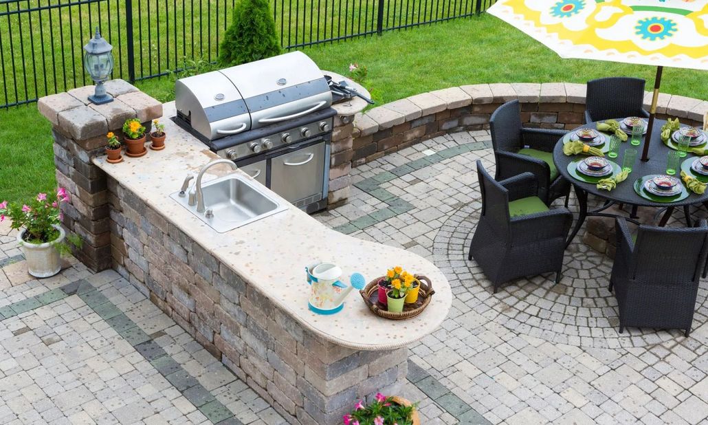 Outdoor patio with grill, sink, and dining table on a brick surface.