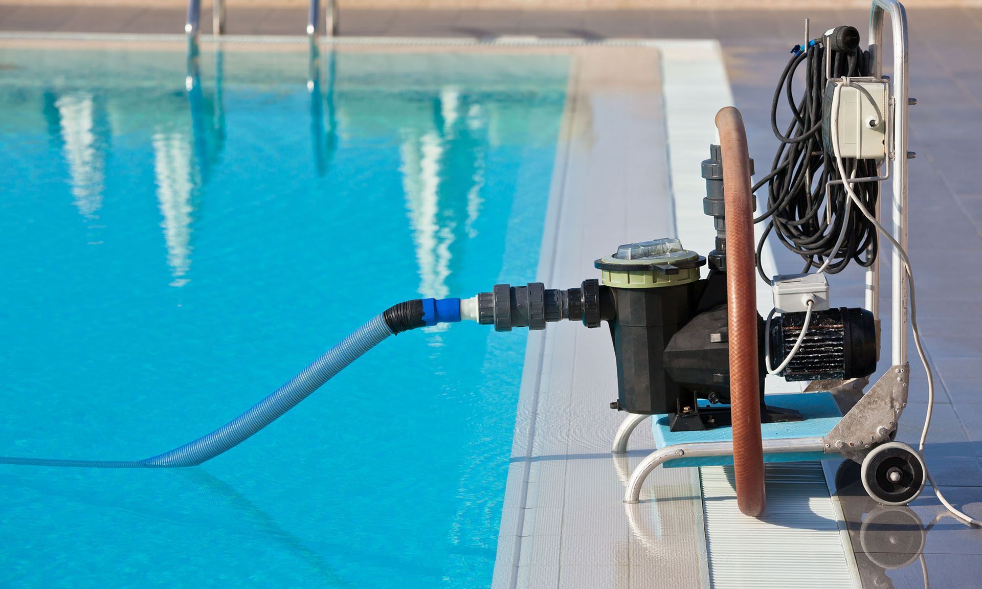 Pool pump and filtration system set up beside a swimming pool, blue water, sunny day.