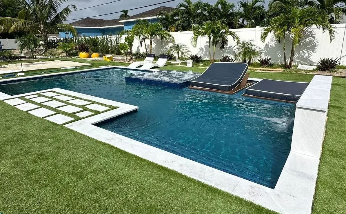Rectangular pool with white tile edging and artificial turf lawn. Dark blue water with floating lounge chairs.
