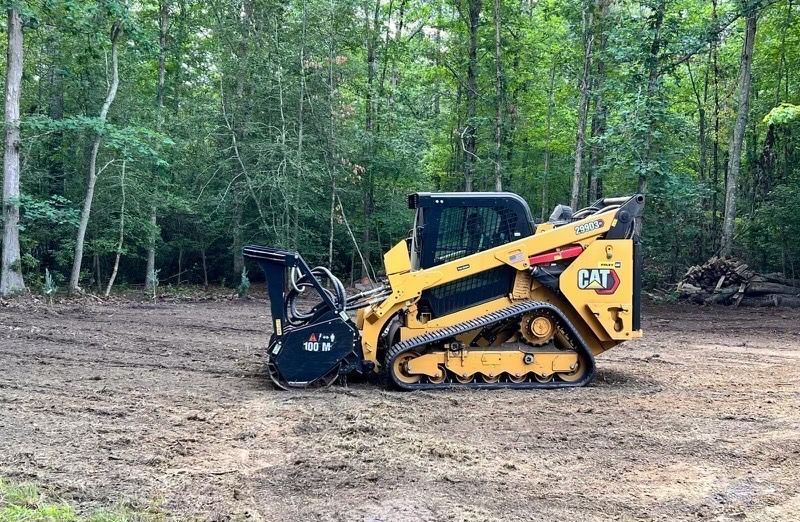 A bulldozer is driving through a dirt field in the woods.