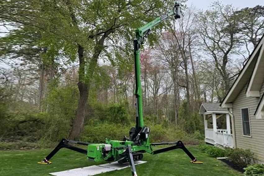 A green spider lift is sitting in front of a house.