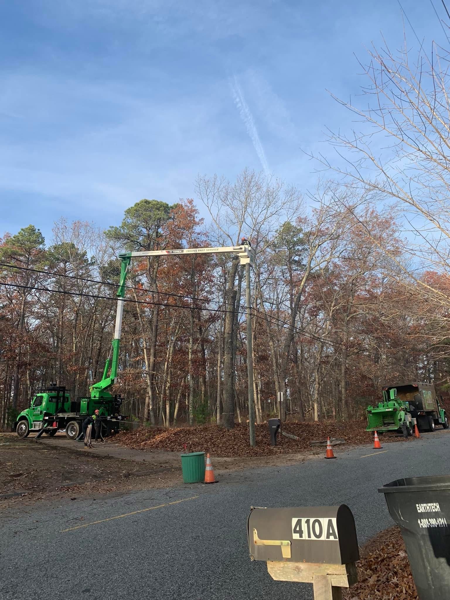 A green crane is working on a power line in the woods.