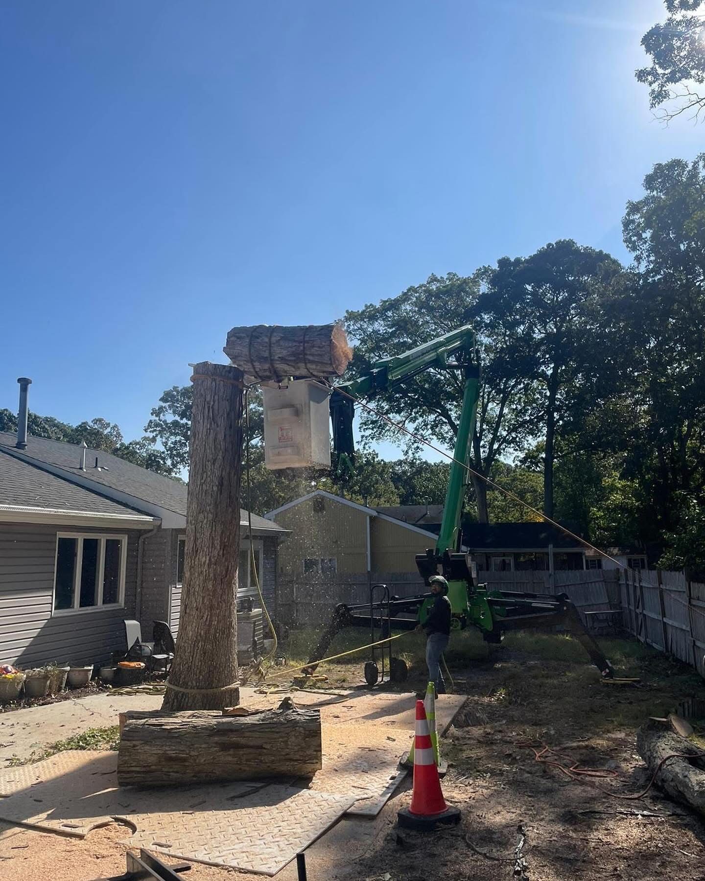 A crane is cutting down a tree in front of a house.