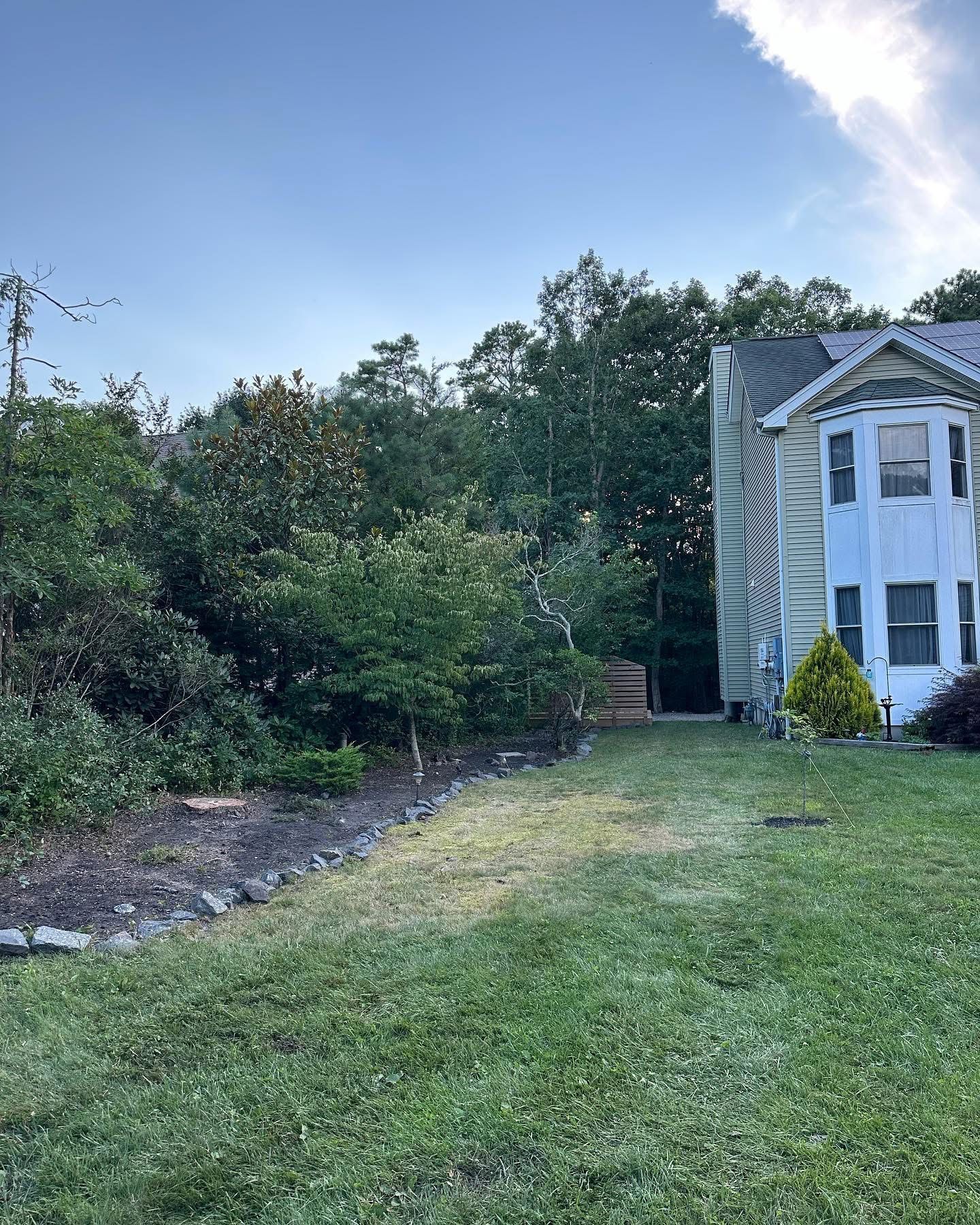 A large white house is sitting in the middle of a lush green field surrounded by trees.