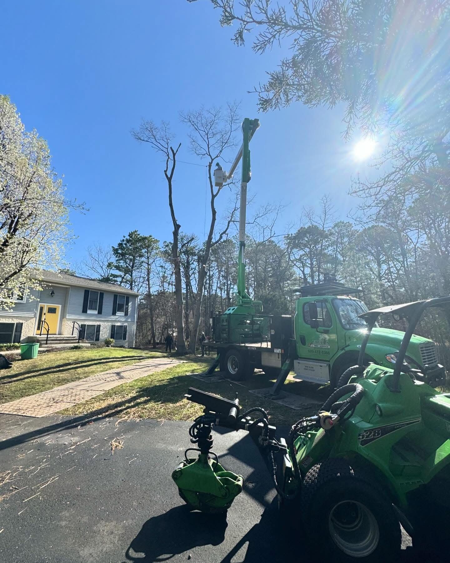A green truck is cutting a tree in front of a house.