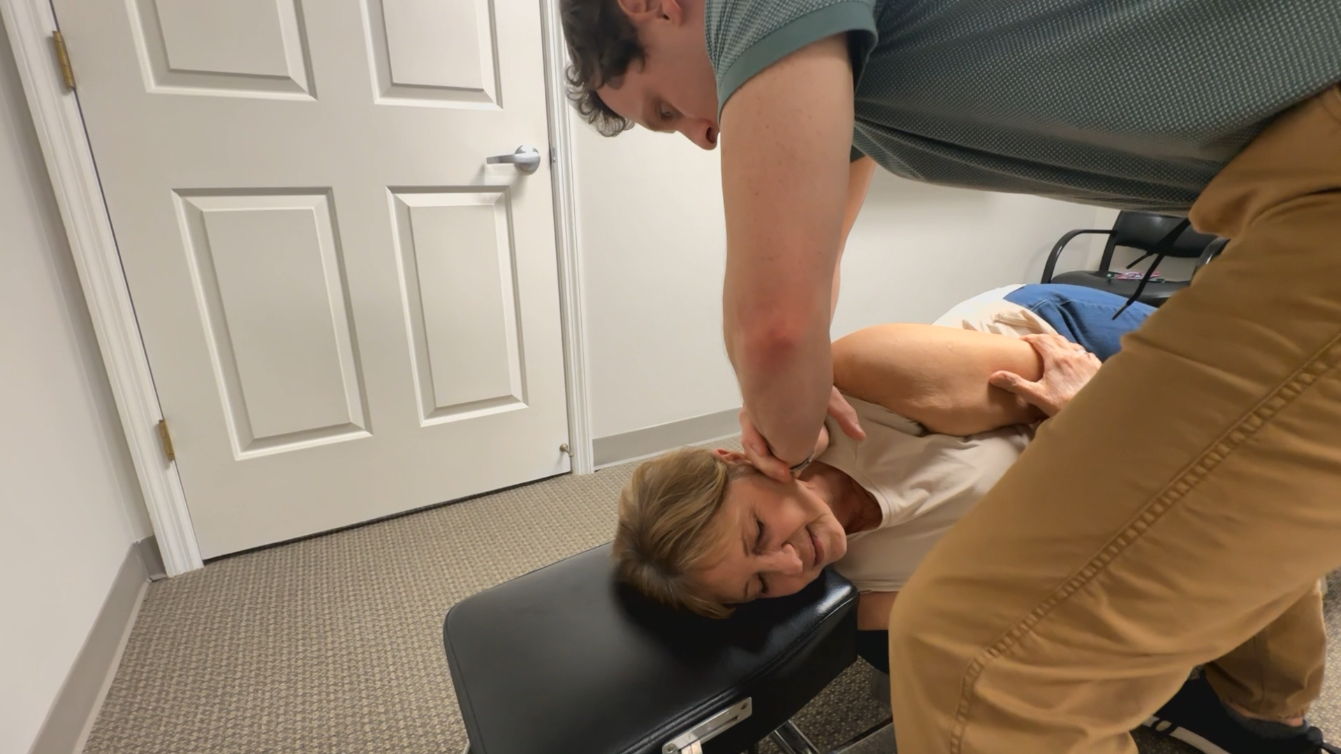 Person receiving a chiropractic neck adjustment on a treatment table in a clinic room