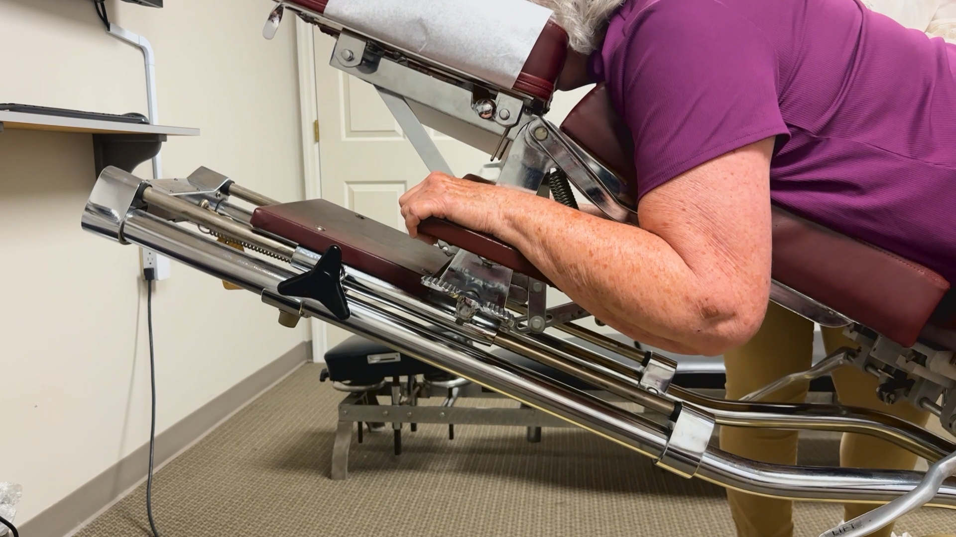 Person leaning into a mechanical treatment chair in a clinic, wearing a purple shirt.