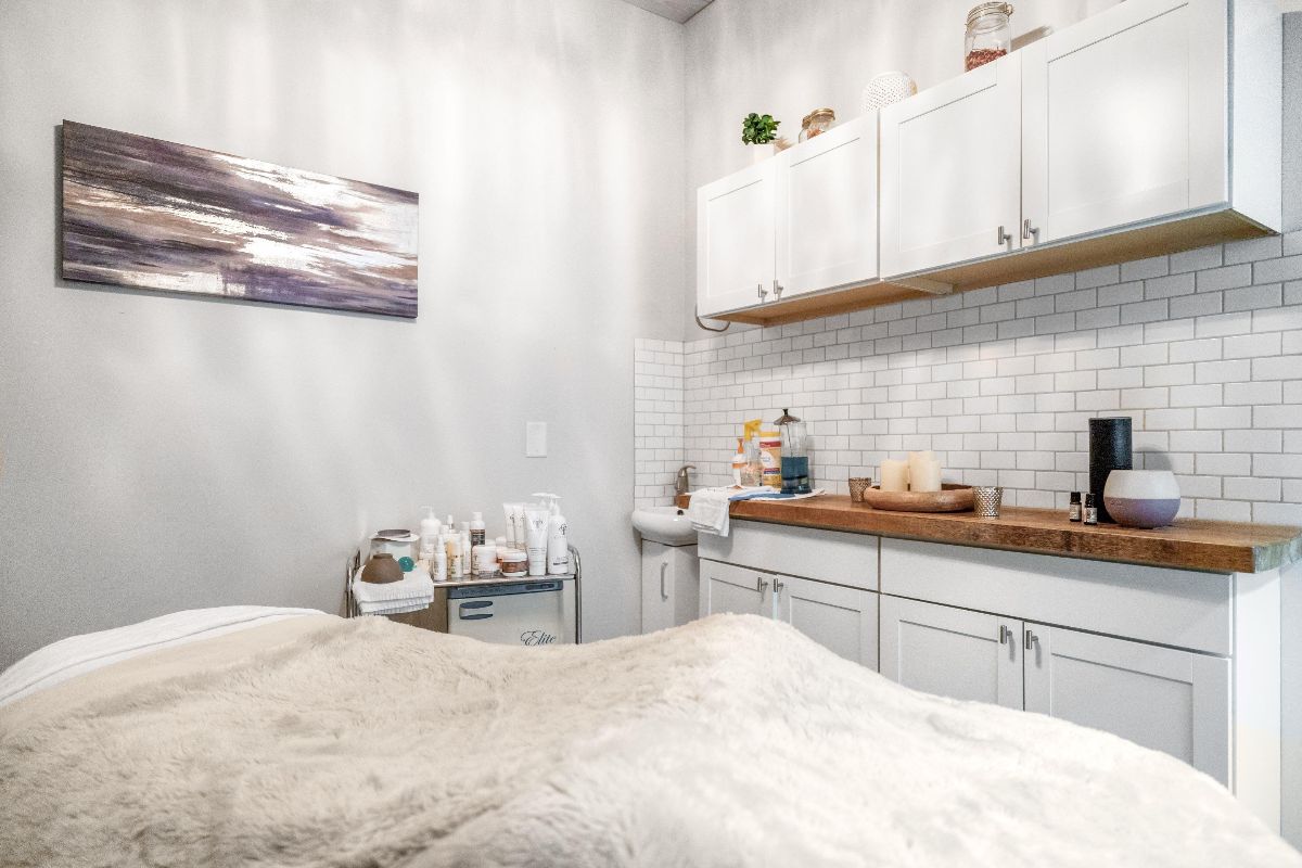 Bright white bedroom with built-in kitchenette, wooden counter, white cabinets, and a bed in the foreground