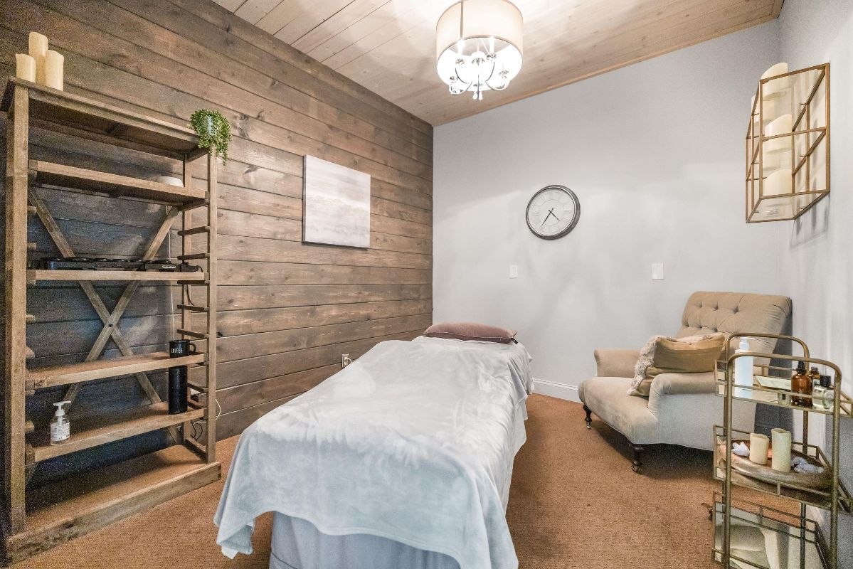 Cozy massage room with a treatment table, wood accents, chair, shelves, and soft lighting