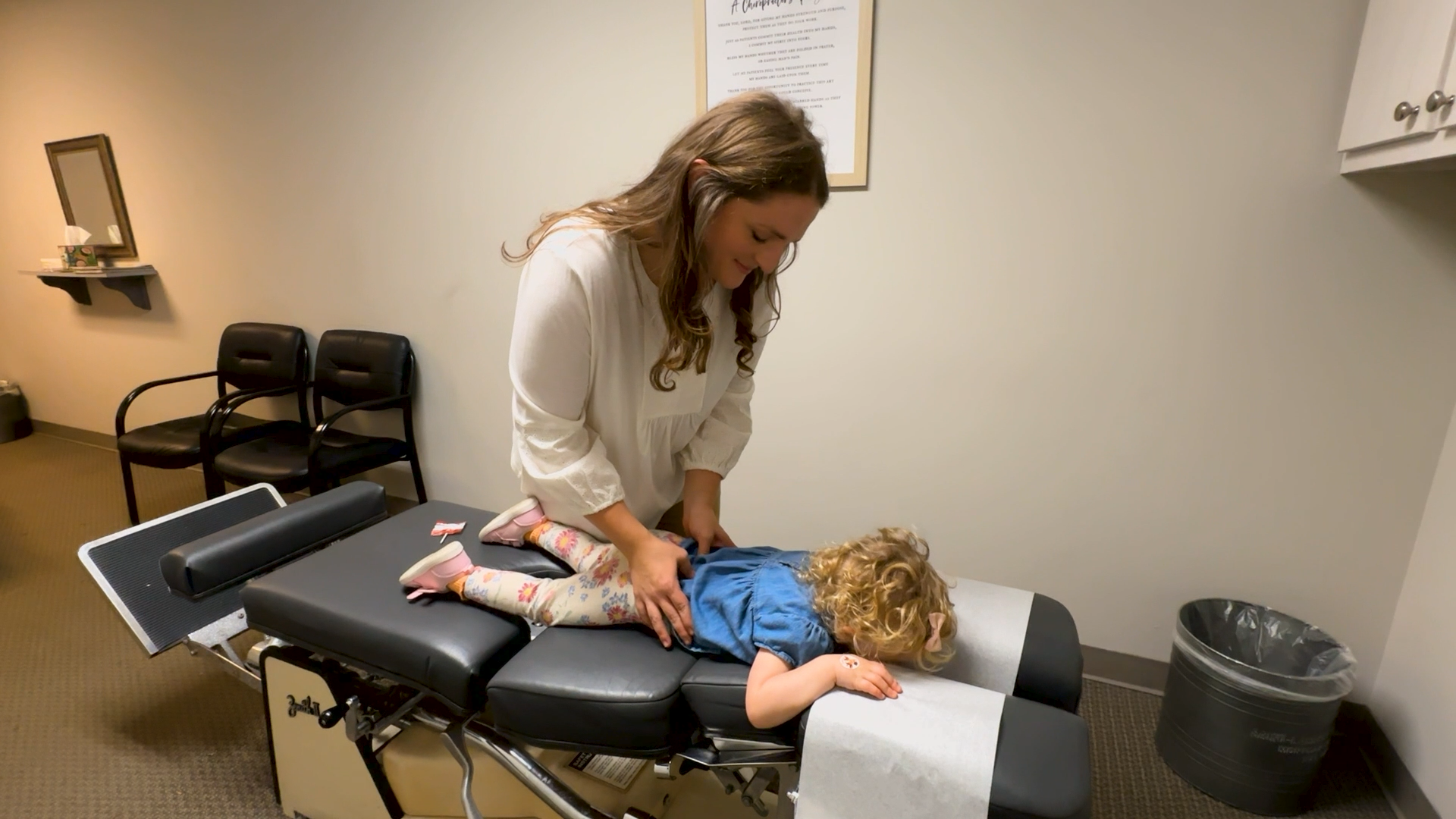 Chiropractor adjusting a child lying face down on a treatment table in a clinic room