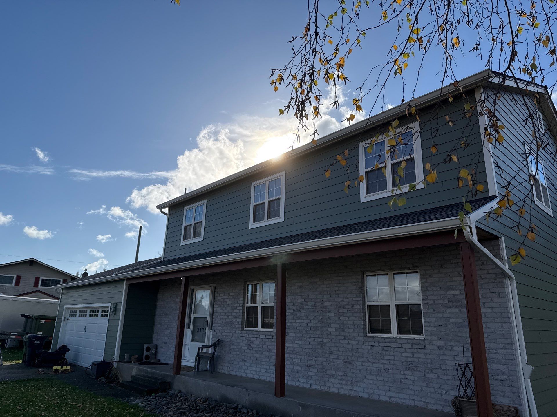 Two-story house with green siding and a porch, sun shining through clouds above.