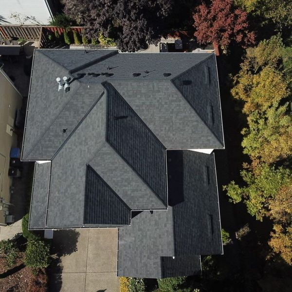 Overhead view of a house with a dark gray shingle roof surrounded by trees with fall colors.