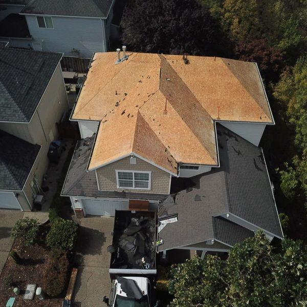 Aerial view of a house with roof partially replaced, showing exposed wooden underlayment and debris.