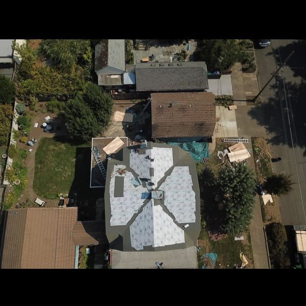 Aerial view of a house undergoing roof replacement. Workers on the roof, materials and tools visible.