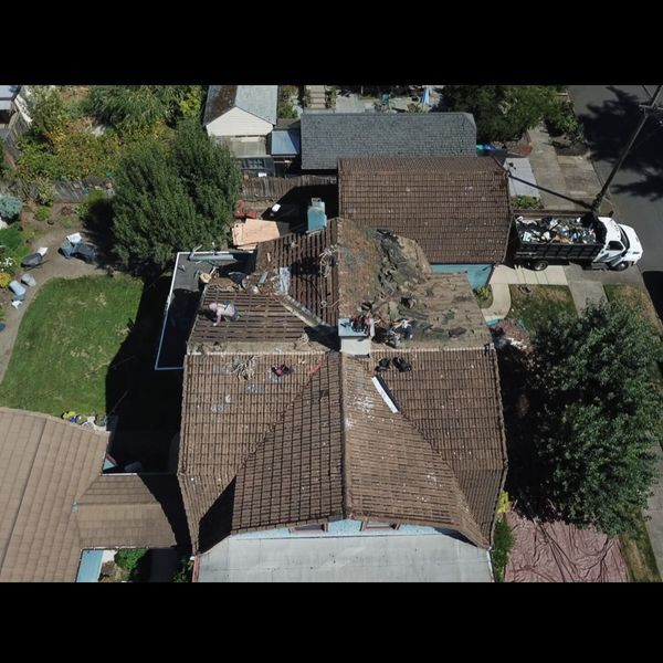Overhead view of house roof being repaired; debris visible. Dump truck parked nearby.