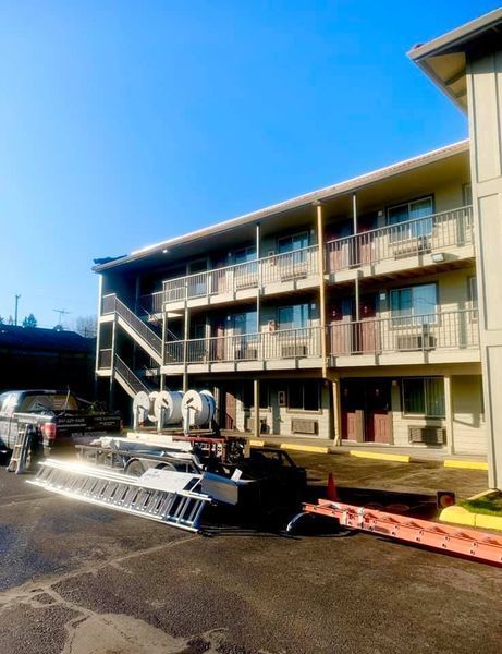 Exterior view of a two-story motel with a clear blue sky, construction equipment in the parking lot.