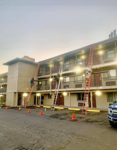Workers on tall ladders repairing a two-story motel. Orange cones line the parking lot.