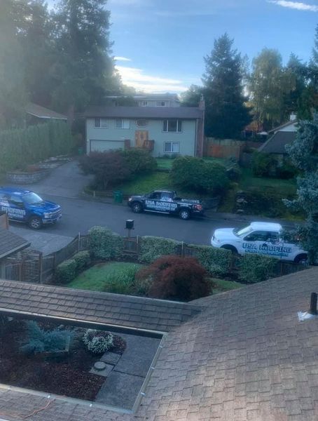 Police vehicles parked on a residential street. A light green house sits behind a driveway and some foliage.