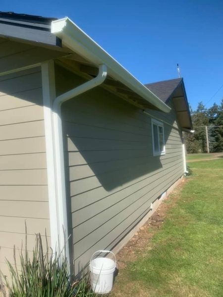 Side view of a house with white gutters, siding, and trim. A white bucket sits on the grass below.