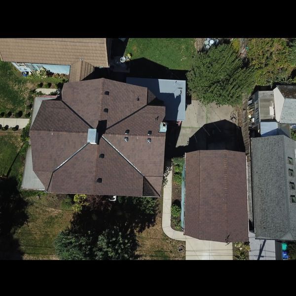 Overhead view of a house with a brown roof and attached garage, surrounded by green grass and trees.