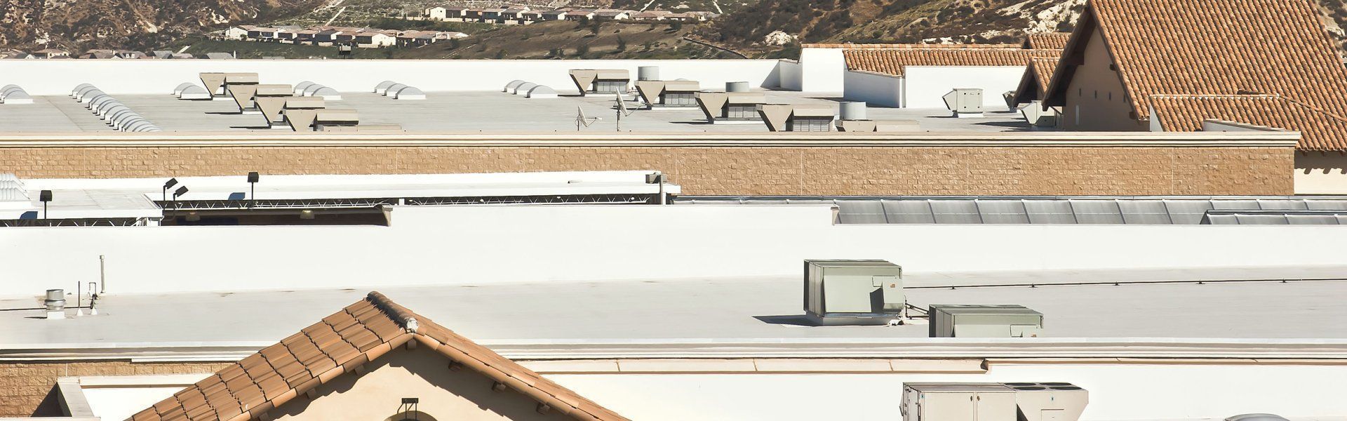 Roofs of buildings with ventilation systems and terracotta tiles. In the background are mountains and a sunny day.