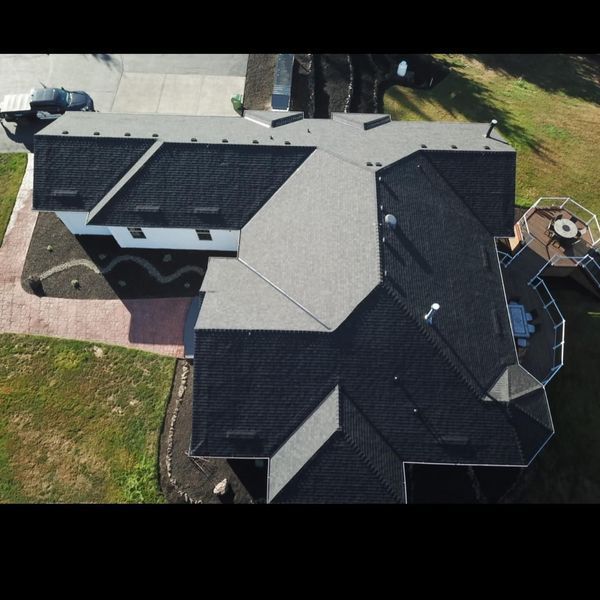 Overhead view of a house with a complex multi-tone roof, surrounded by lawn and driveway.