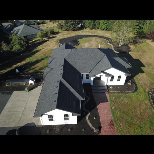 Aerial view of a white house with a dark gray roof, surrounded by green grass and landscaping.