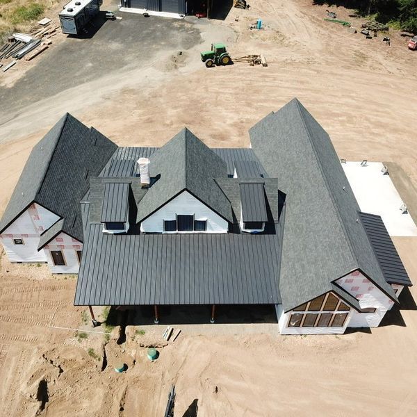 Aerial view of a house under construction with a dark gray roof and white siding in a dirt field.