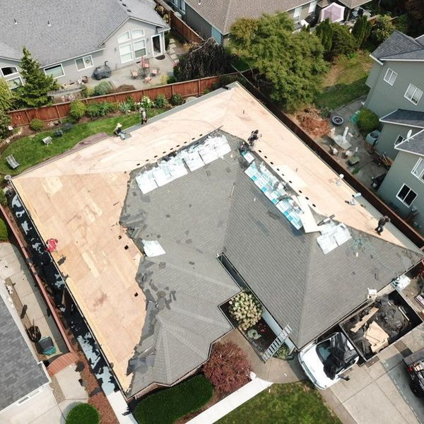 Aerial view of a roof being repaired. Workers on roof, partially covered, materials and truck present.