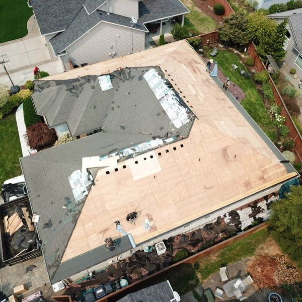 Aerial view of a house roof undergoing repair. The roof is partially torn off with new plywood installed.