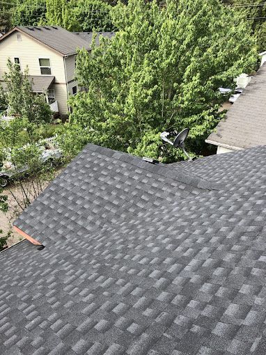 Dark gray asphalt shingle roof with houses and trees visible in the background.