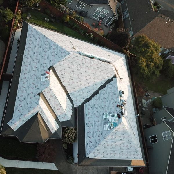Overhead view of a house roof partially covered with roofing underlayment, showing a construction project in a residential area.