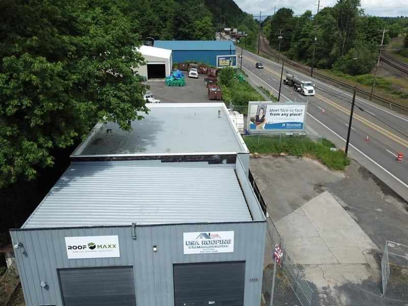 Aerial view of industrial buildings with gray roofs, next to a highway.