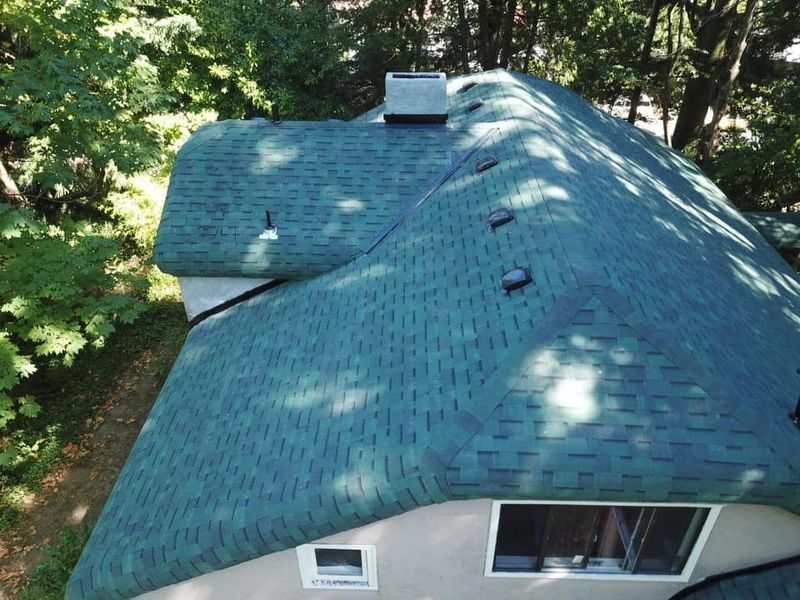 Green shingled roof with a chimney and a small window.