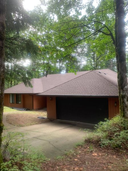 Brown house with a garage, surrounded by trees, on a concrete driveway.