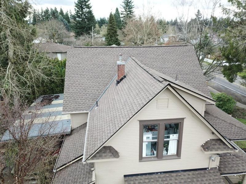 Overhead view of a house with a brown shingled roof, chimney, and beige siding.
