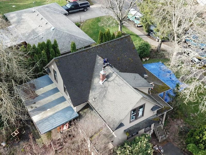 Overhead view of a house with a dark gray roof, blue tarp, and a person working on the roof.