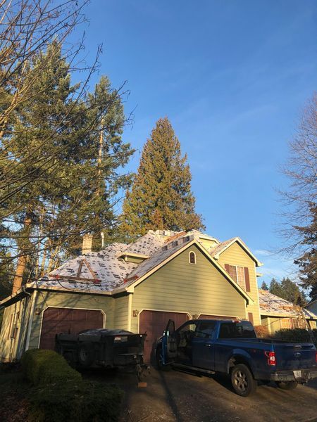 Green house with snow-covered roof, brown garage doors, and blue pickup truck in driveway under a clear blue sky.