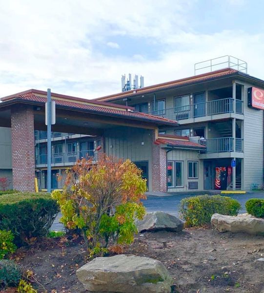 Exterior of Quality Inn, two-story building with balconies, brick columns, brown roof, and landscaping.