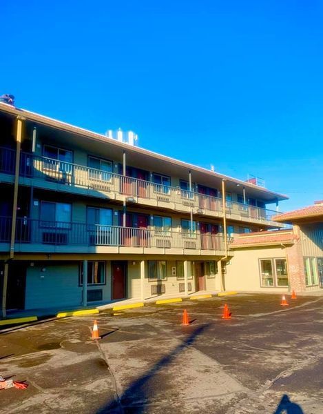Motel exterior with two levels of rooms and balconies; orange traffic cones in parking lot. Blue sky.