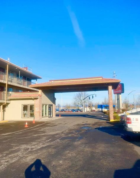 Hotel entrance with archway, blue sky. Paved driveway, building on left, parked car on right.